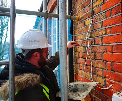 Construction worker in hard hat repairing brick wall, showcasing restoration efforts for old buildings, relevant to Edwardian and Victorian house renovations.