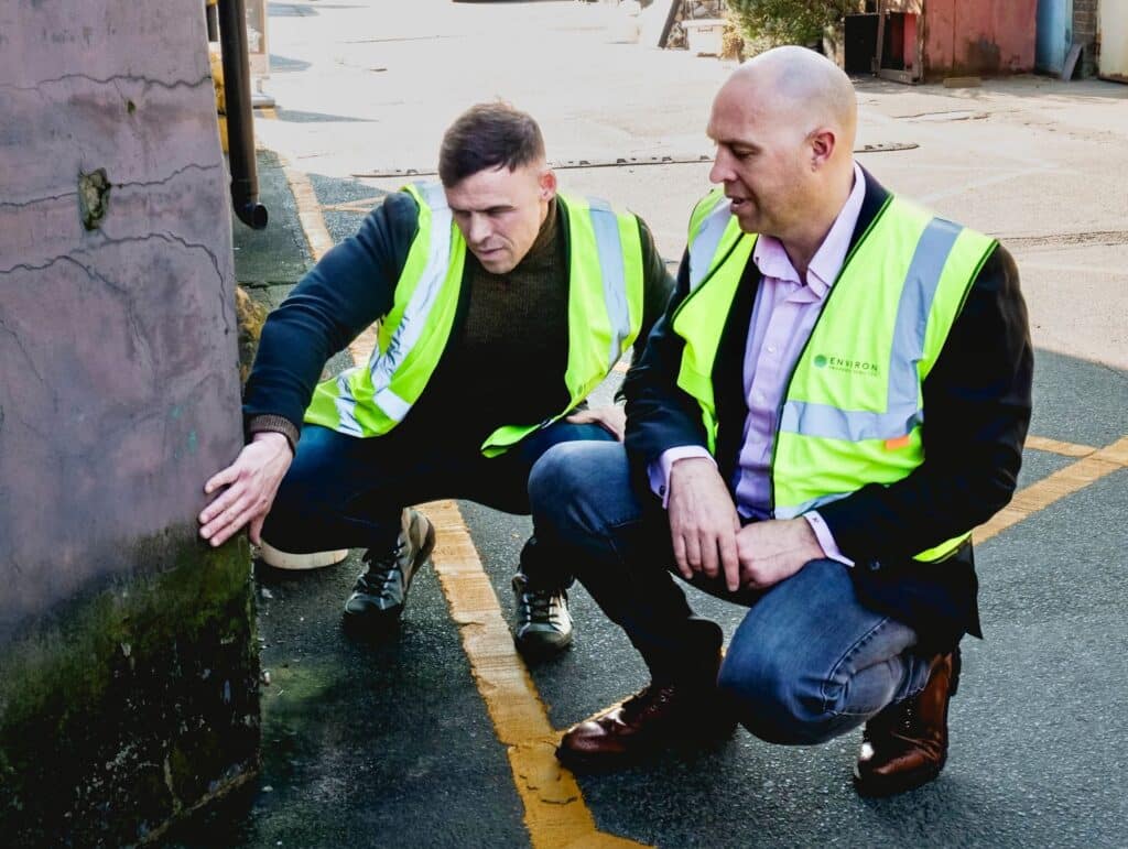Two professionals in high-visibility jackets inspecting damp patches on a brick wall, highlighting the importance of identifying moisture issues in home restoration.
