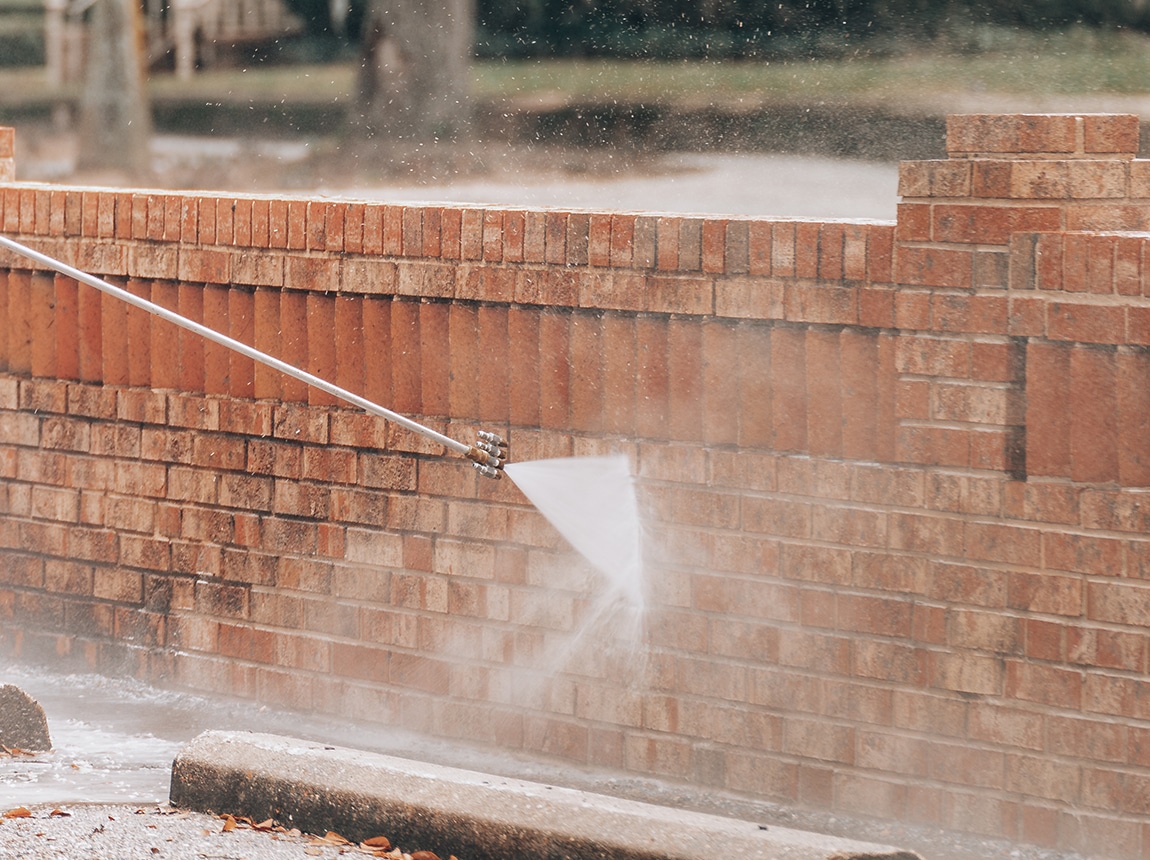 Person using a pressure washer to clean a brick wall, showcasing effective brick cleaning techniques for property maintenance.