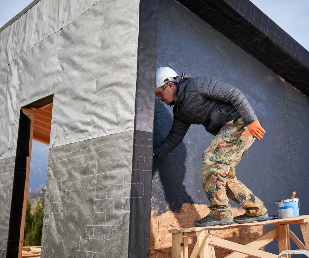 Construction worker applying damp-proof membrane to exterior wall, enhancing moisture protection during building process.