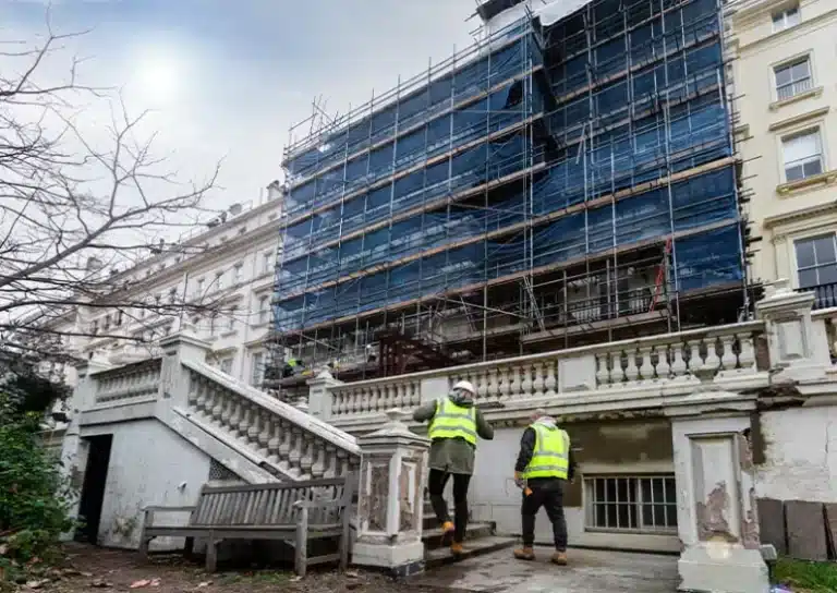 Construction workers in high-visibility vests inspecting a building under renovation, surrounded by scaffolding and a partially visible staircase, highlighting property maintenance and restoration services in London.