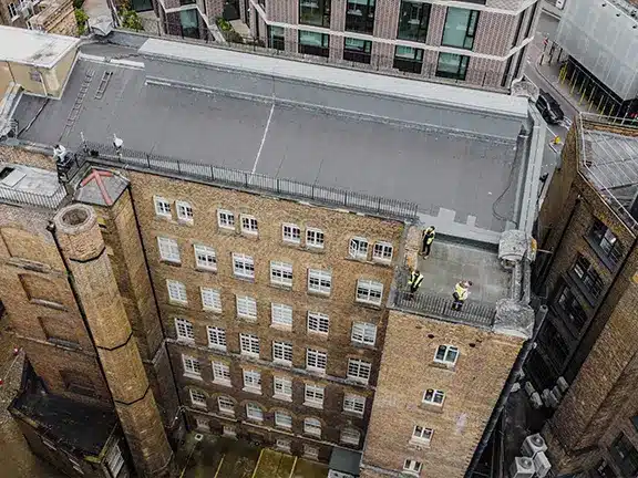 Aerial view of a historical brick building with restoration workers in safety gear on the roof, showcasing heritage restoration efforts by Environ Restoration Services.