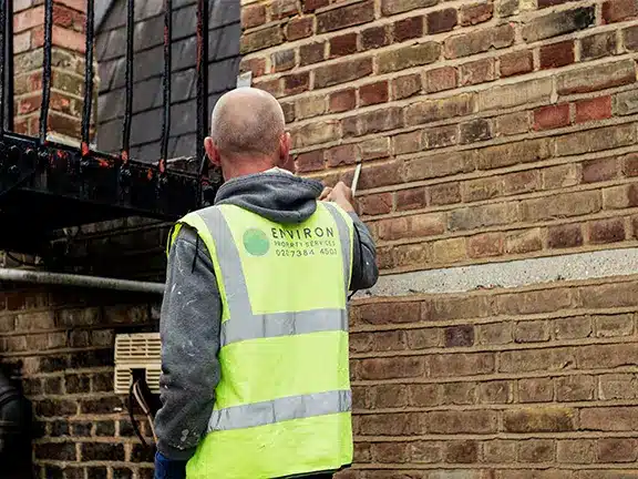 Worker in high-visibility vest applying lime mortar to brick wall during repointing process for heritage property restoration by Environ Restoration Services.