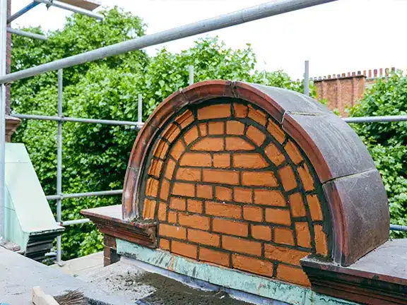 Repointed brick arch in a heritage building, showcasing traditional masonry techniques and lime mortar application, with scaffolding and greenery in the background.