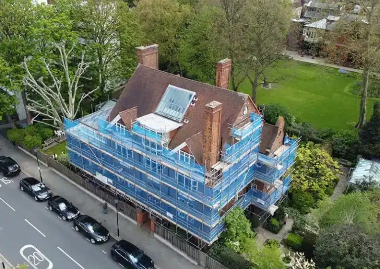 House undergoing renovation with scaffolding, surrounded by greenery and parked cars, illustrating property maintenance and damp prevention in London.