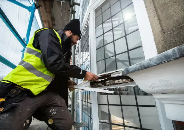Skilled tradesman repairing timber sash window, restoring original form and functionality, wearing safety gear and working on decaying frame.