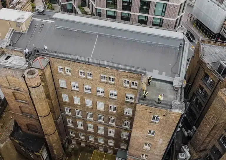 Drone roof survey in London, showing workers inspecting a building's rooftop and adjacent structures, highlighting advanced maintenance techniques for efficient property assessments.