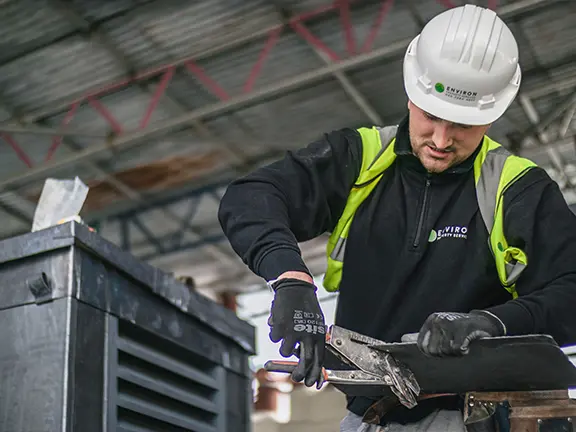 Construction worker in a hard hat and safety gear using tools to maintain a period building, showcasing expertise in restoration services by Environ Restoration.