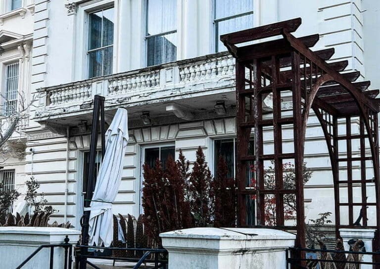 Georgian house exterior with ornate balcony, partially covered by a white umbrella, and a wooden trellis in the foreground, illustrating the architectural features relevant to restoration services.