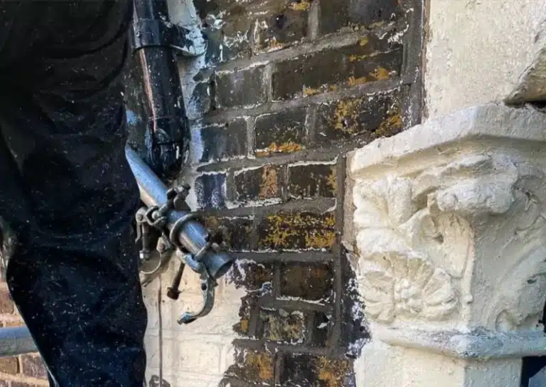 Worker using restoration equipment on a historic brick wall with detailed stonework, highlighting renovation efforts for listed buildings in London.