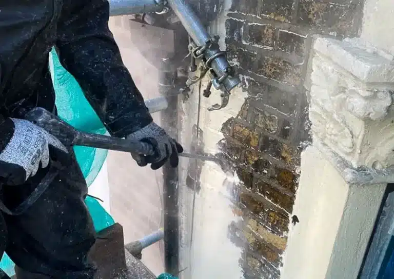 Worker using a power tool to restore brickwork on a historic building, showcasing renovation techniques for listed buildings in London.