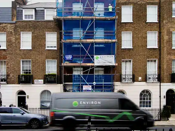 Scaffolding on a building facade in London with an Environ Restoration Services van passing by, showcasing ongoing Section 20 works for property maintenance and restoration.