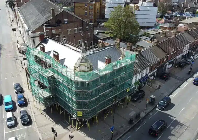 Building under renovation with scaffolding and green mesh covering, located in a London street scene, showcasing urban development and property maintenance.