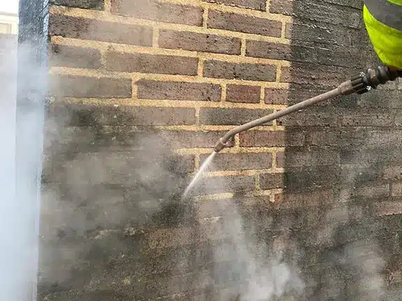 High-pressure cleaning of brick facade, removing dirt and grime, demonstrating facade cleaning services by Environ Restoration Services.