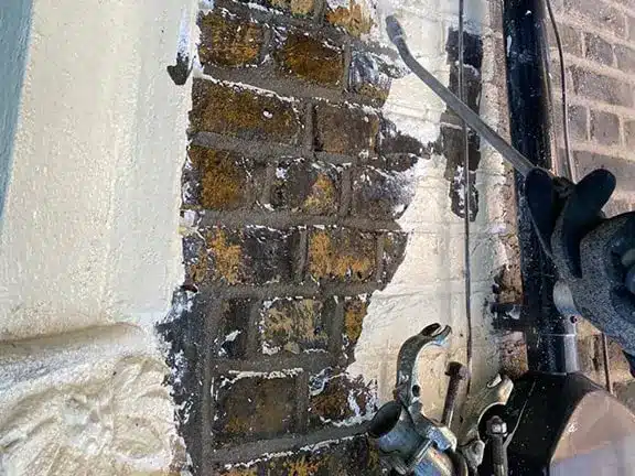 Brick paint removal process revealing original brickwork, showcasing restoration tools and techniques for stone wall restoration.