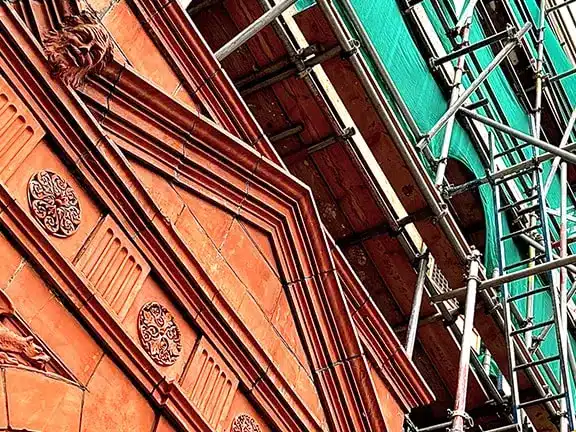Detailed view of ornate architectural features on a listed building, showcasing restoration work with scaffolding and protective sheeting in place.