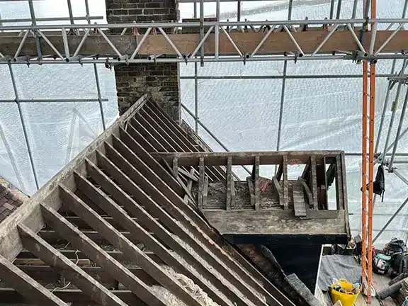 Roof structure undergoing repair with scaffolding and protective sheeting, showcasing maintenance work on a period property.