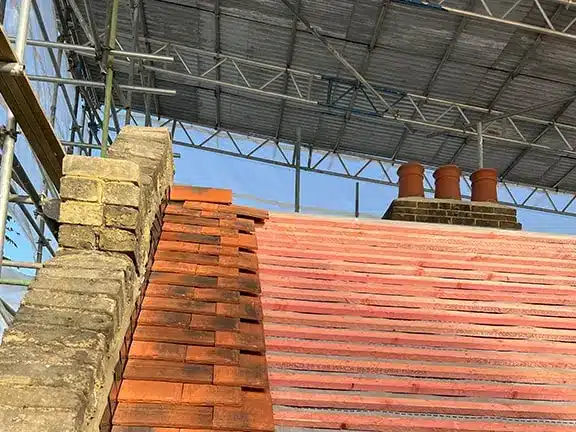 Roof under repair showcasing traditional red tiles, masonry chimney, and scaffolding, representing heritage property restoration by Environ Restoration Services.