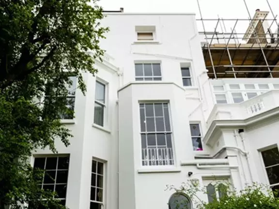 Restored traditional building facade in London, showcasing white exterior with large windows, surrounded by greenery and scaffolding for ongoing refurbishment.
