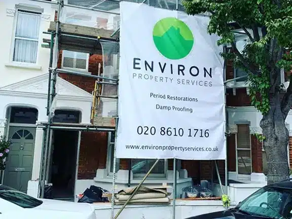 Environ Property Services banner on scaffolding, advertising period restorations and damp proofing, set against a backdrop of a traditional London building under refurbishment.