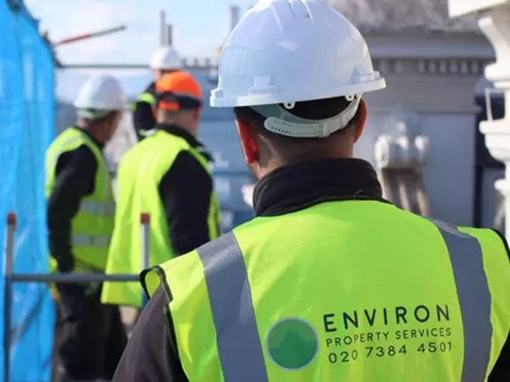 Team of Environ Restoration Services professionals wearing safety gear and high-visibility vests, engaged in damp proofing work on a property site.