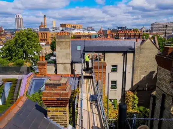 View of London rooftops with scaffolding and a restoration specialist working on a building, showcasing traditional architecture and urban landscape.