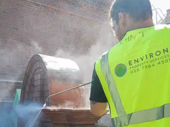 Restoration specialist from Environ Restoration Services using a pressure washer on a traditional building façade, surrounded by mist and dust.
