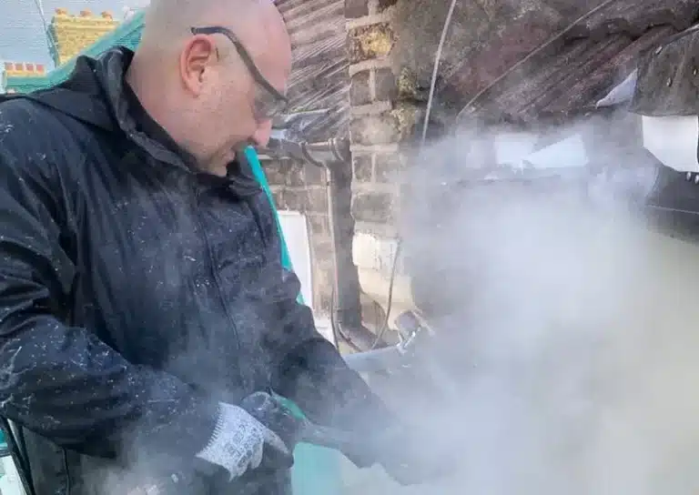 Man using a steam cleaning tool for building restoration, surrounded by mist and historical architecture elements, showcasing Environ Restoration Services' commitment to heritage renovation.
