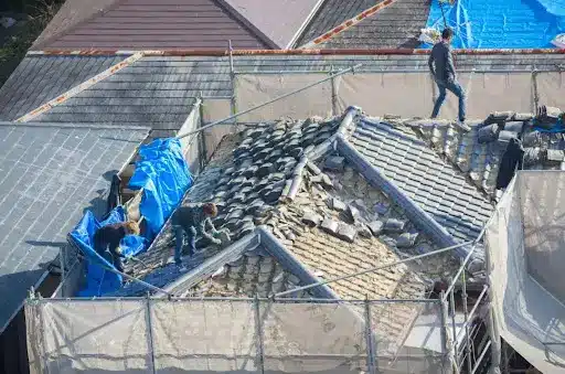 Roofers repairing a historic tiled roof with scaffolding and tarpaulins, showcasing expert craftsmanship in period property restoration.