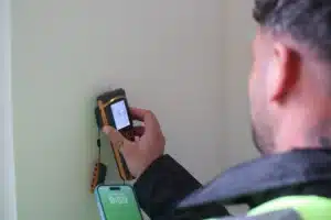 Professional using a damp meter to assess moisture levels in a wall, relevant to brickwork restoration and maintenance.