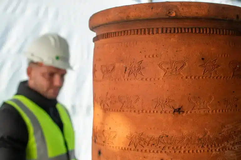 Restoration expert examining intricately designed terracotta pot with historical engravings, showcasing attention to detail in heritage preservation.