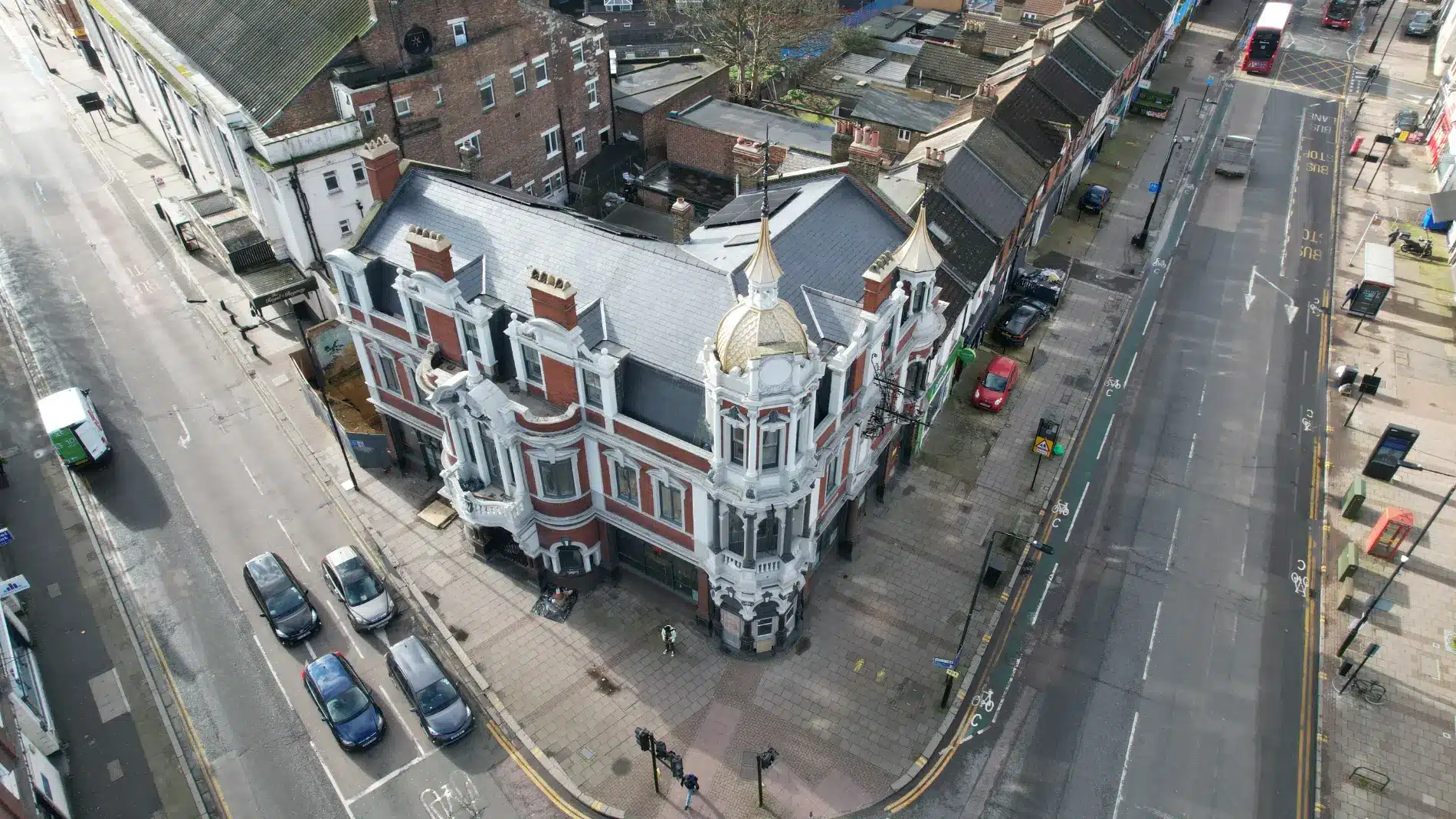 Historic building with ornate architecture and a golden dome, situated at a street intersection in London, surrounded by modern vehicles and residential properties, illustrating the challenges of heritage restoration.