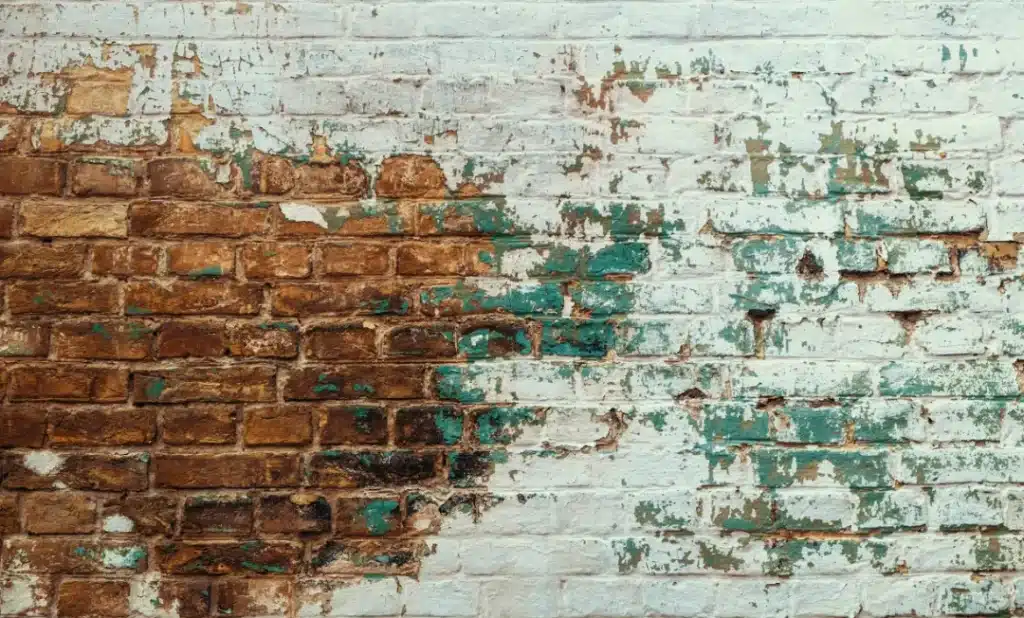 Weathered brick wall with peeling paint, showcasing stains from dirt, mould, and mildew, relevant to cleaning and restoration techniques for brick surfaces.
