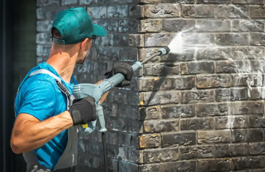 Person using a pressure washer to clean exterior brick wall, demonstrating effective brick cleaning techniques for maintenance.