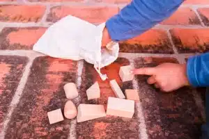 Hand reaching into a bag, retrieving cleaning tools, and pointing at stained brick surface, illustrating effective brick cleaning methods.
