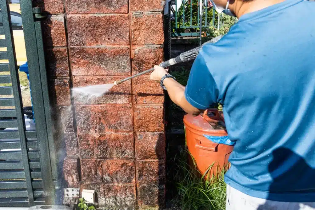 Person using a pressure washer to clean brick wall, demonstrating effective brick maintenance techniques for homeowners.