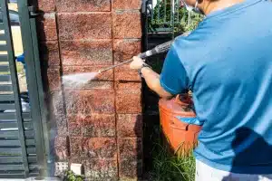 Person using a pressure washer on brick wall for cleaning, illustrating effective brick maintenance techniques relevant to winter protection and restoration.