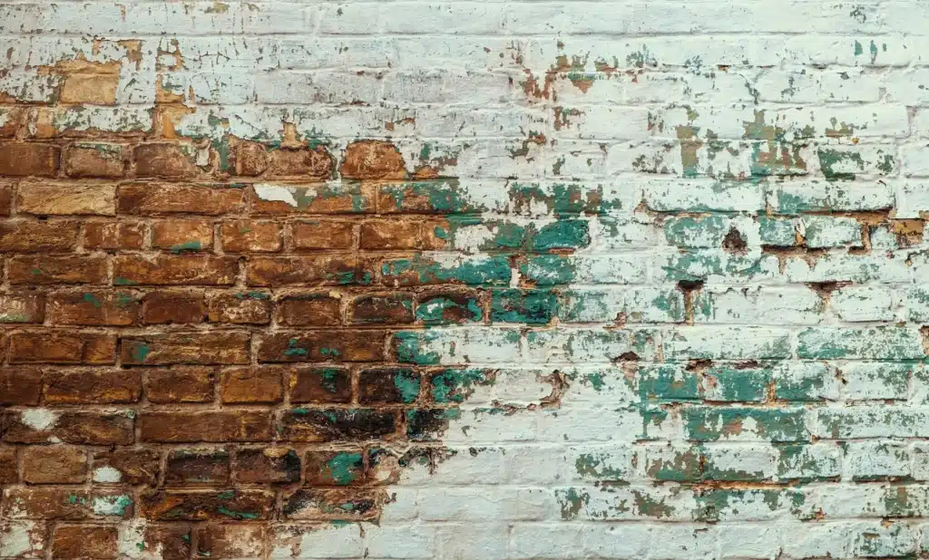 Brick wall with peeling paint, showcasing layers of deteriorating paint and exposed brick, relevant to paint removal and brick restoration services.