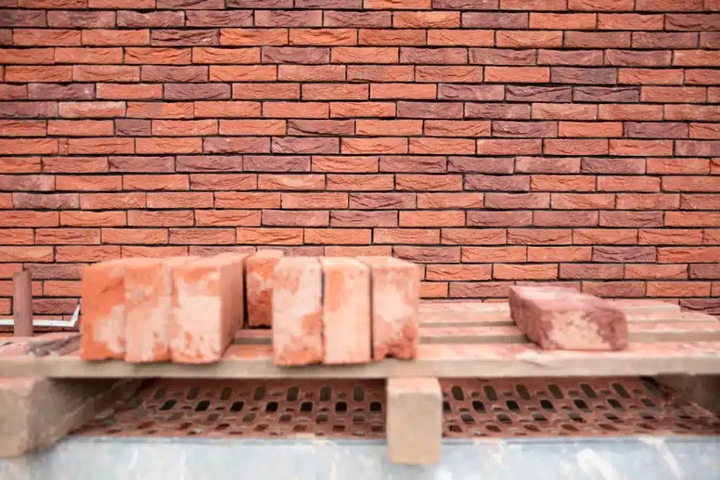 Bricks displayed on a wooden pallet against a textured brick wall, showcasing various types of bricks relevant for construction and restoration projects.