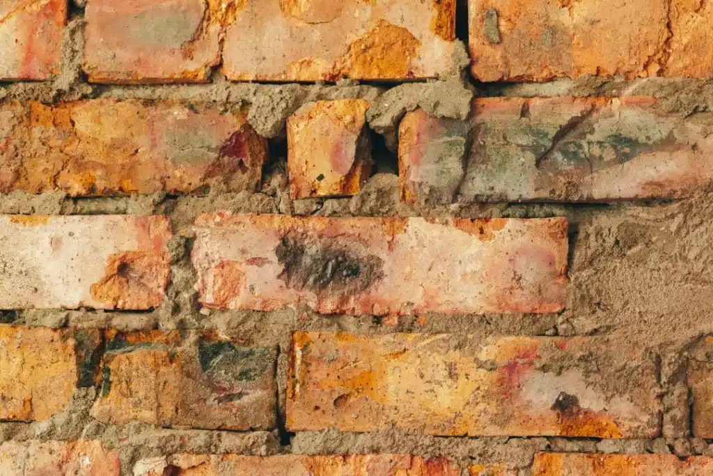 Close-up of damaged brick wall showing cracked mortar joints and varying brick colours, illustrating the need for evaluation and repair in preparation for effective brick cleaning.