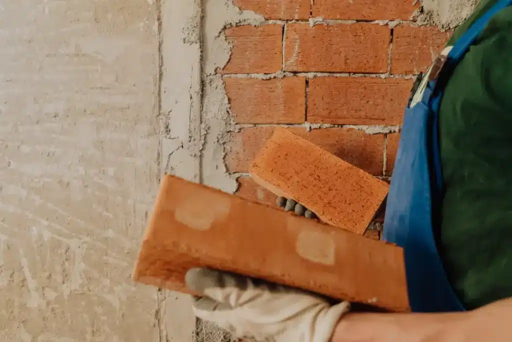 Person holding brick near cleaned brick wall, demonstrating brick restoration techniques relevant to property maintenance and landscaping protection.