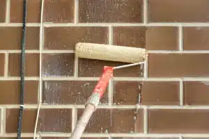 Roller applying cleaning solution to brick wall for restoration and maintenance.