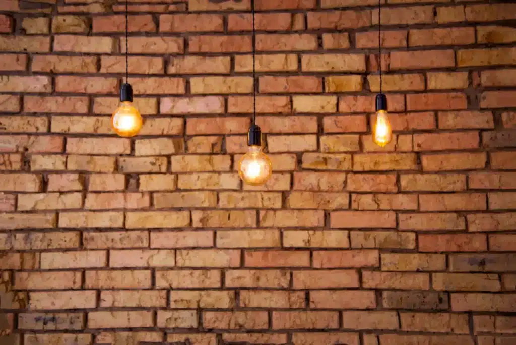 Hanging light bulbs illuminating a textured brick wall, showcasing the aesthetic appeal of restored brickwork relevant to professional cleaning and maintenance services.
