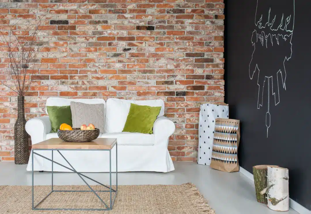 Interior space featuring exposed brick wall, white sofa with green cushions, wooden coffee table with fruit bowl, and decorative elements, highlighting the importance of maintaining clean and preserved brickwork.